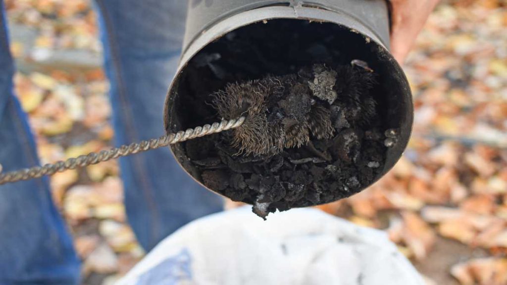 Een schoorsteenveger verwijdert al het roet en de teer uit de schoorsteen.