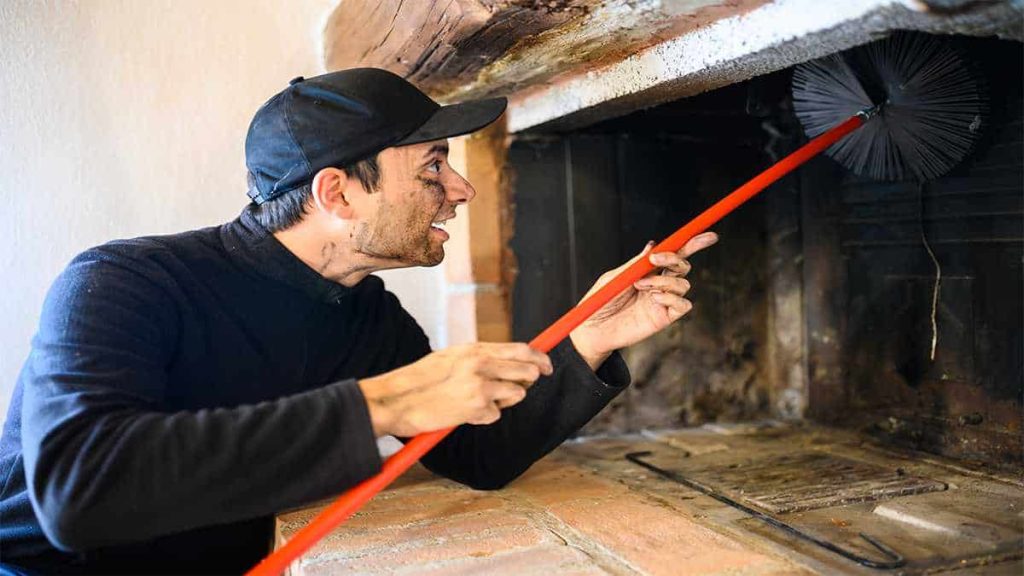 Vakman die de schoorsteen van beneden schoonmaakt, heeft roetvlekken op zijn gezicht en handen.