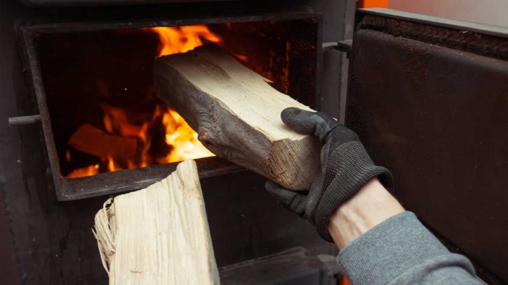 Vers hout die in een brandende houtkachel met open deur wordt gedaan.