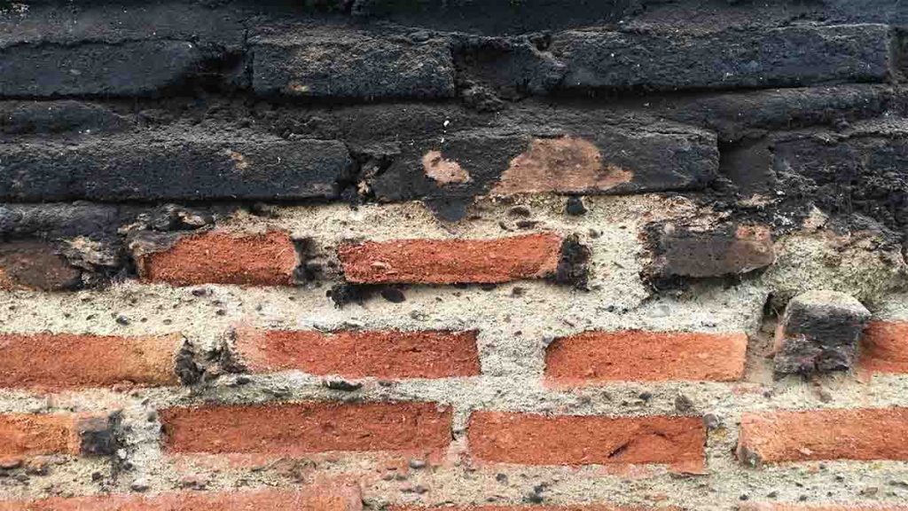 Een bakstenen muur met aan de onderkant goede bakstenen en aan de bovenkant bakstenen die bedekt zijn met roet.